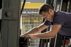 Técnico manipulando un componente frontal de una carretilla elevadora industrial mientras realiza una revisión mecánica.